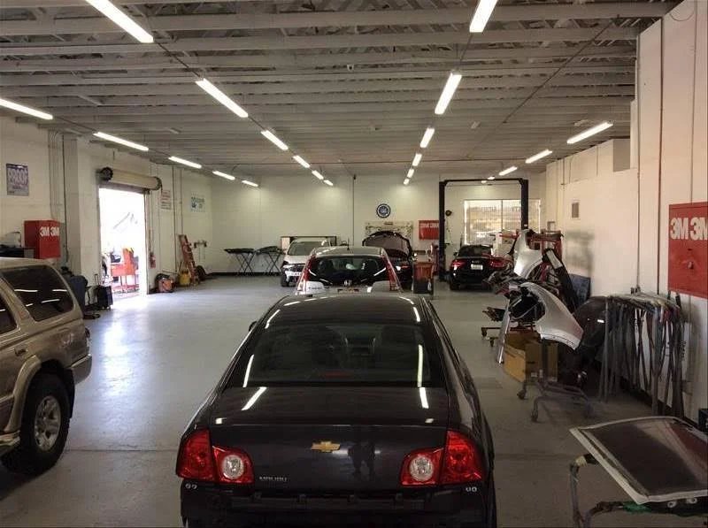 Repair bays with a dark Chevy sedan, parts carts and equipment